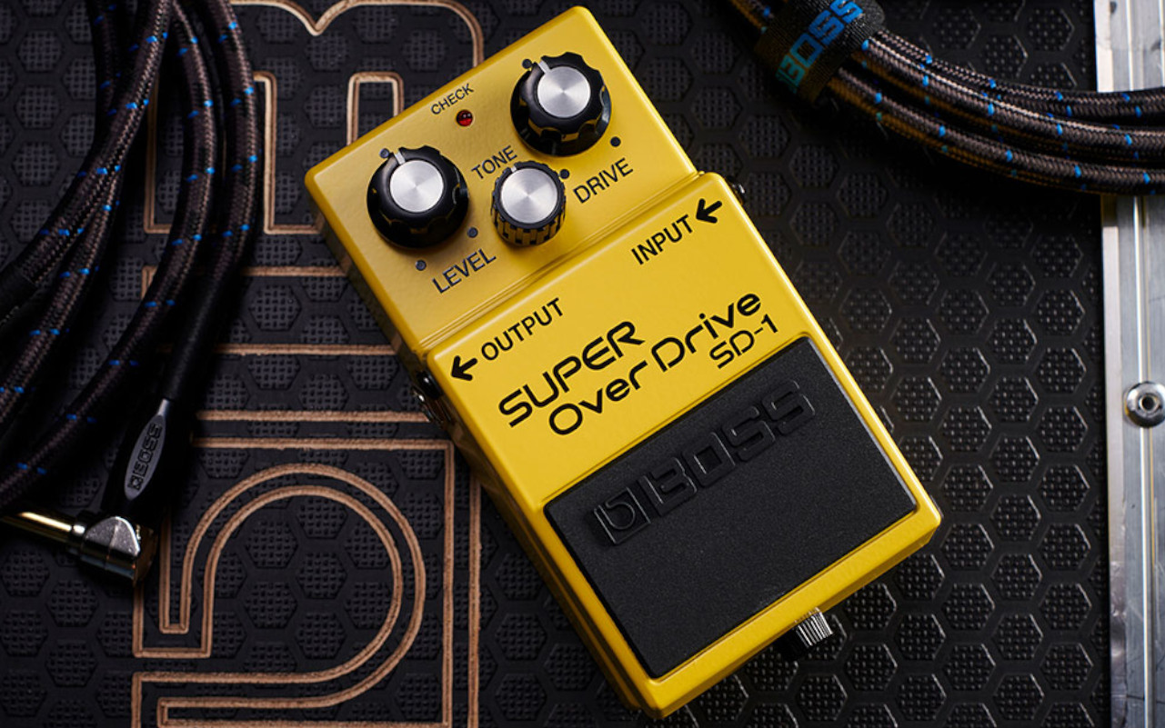 A imagem mostra um boss sd-1 sobre uma caixa e dois cabos